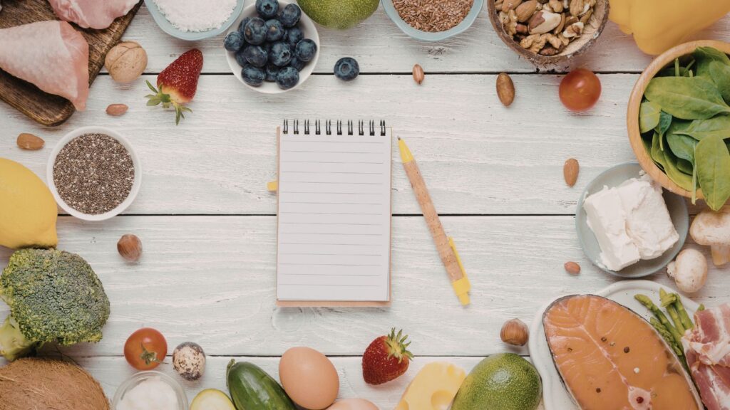 Notatnik otoczony produktami spożywczymi, który symbolizuje planer jedzenia.