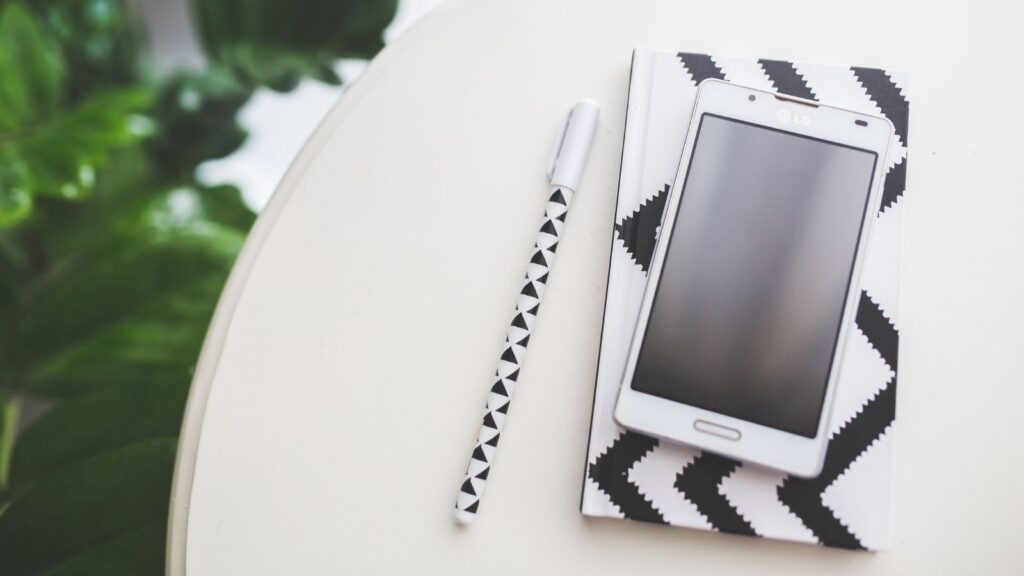Telefon, długopis i notes na białym stole.