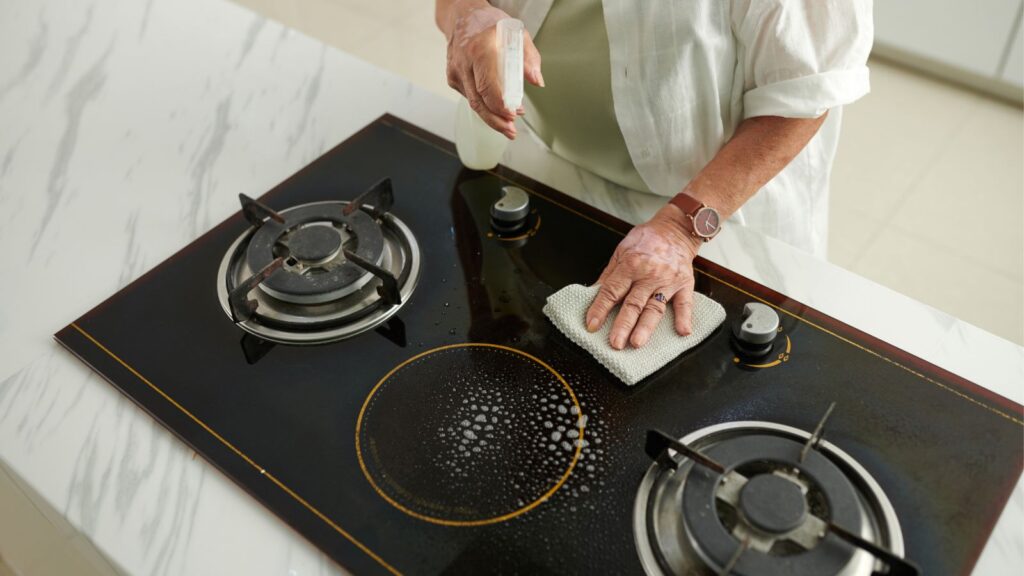 Kobieta sprząta kuchenkę aby usunąć tłuszcz i tłusty nalot gromadzący się podczas gotowania.