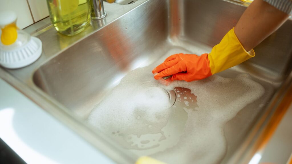 Kobieta czyści zlew po przygotowaniu posiłków, aby zapobiec gromadzeniu się zabrudzeń.